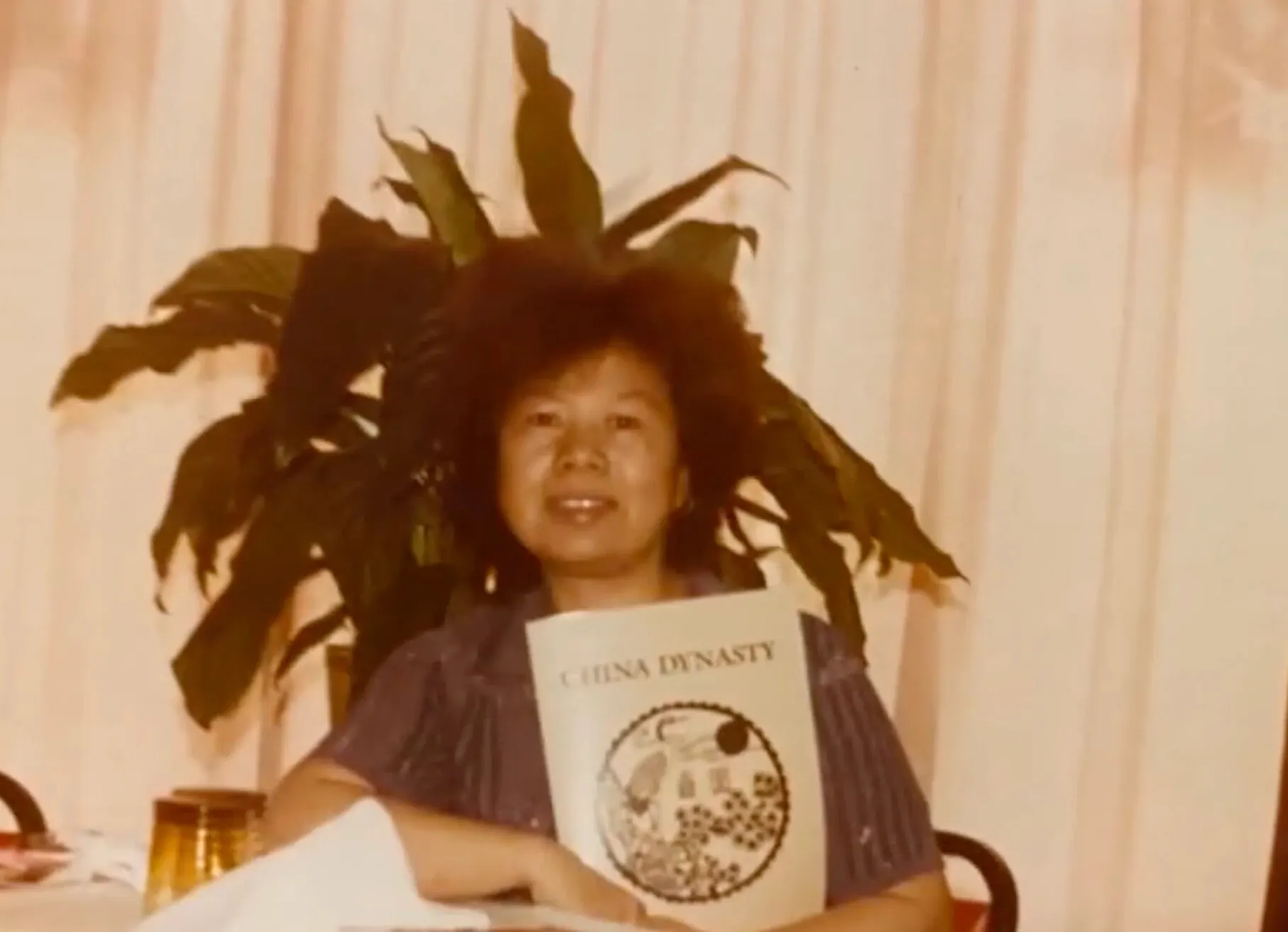 Holding China Dynasty’s very first menu, with a round illustrated cover, in front of a potted plant