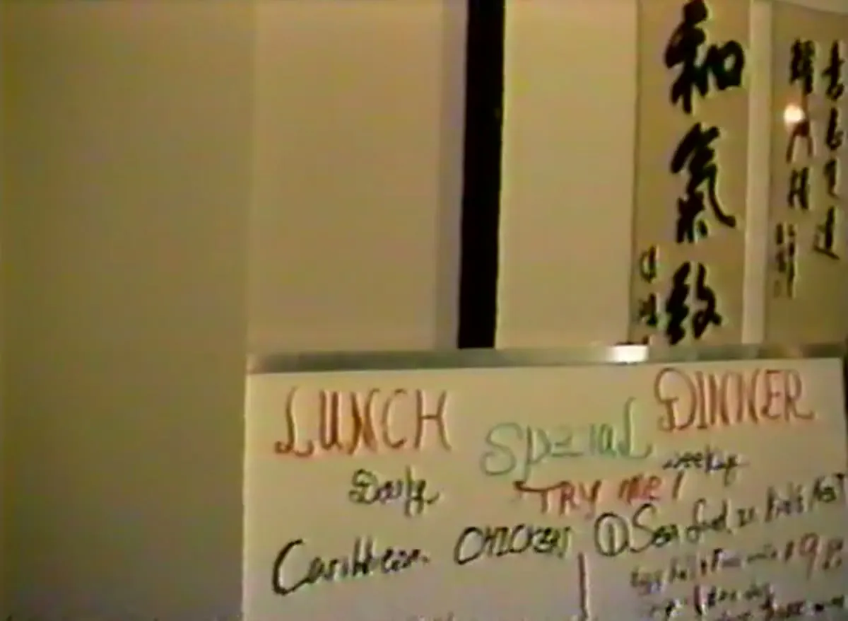 The calligraphy wall with a laughing Buddha painting and a handwritten lunch and dinner specials board, 1989